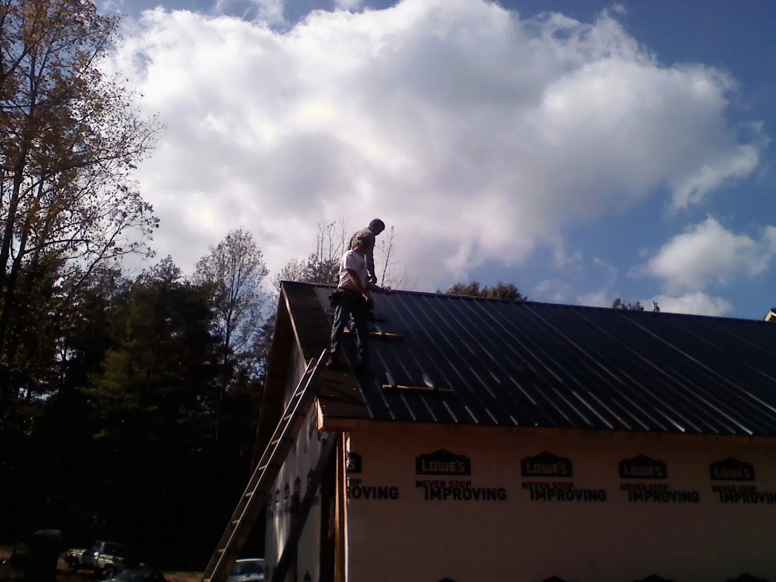 Roofer fastening dark metal panels high against a cloudy sky, from a Roof Inspection job in Willow Springs