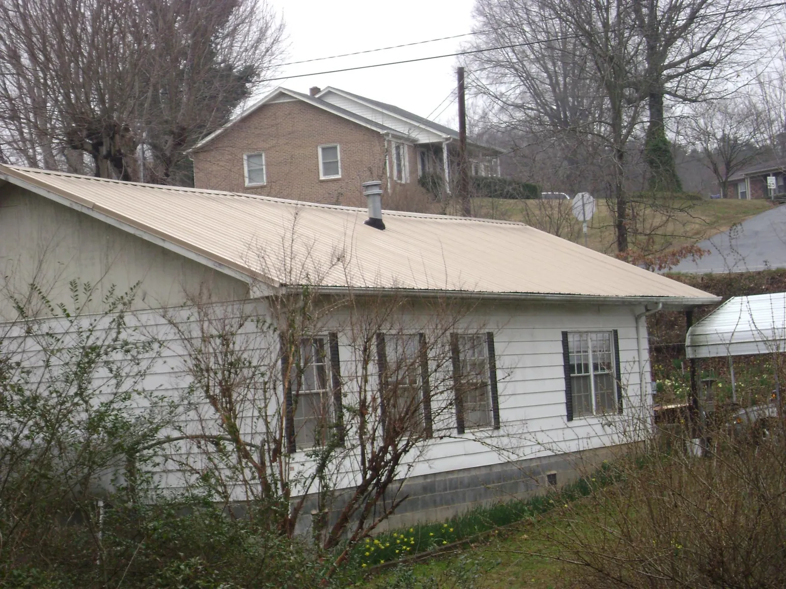 Tan metal roof on a white sided house set into a hillside — Commercial Roofing by Roofing Brothers in Willow Springs